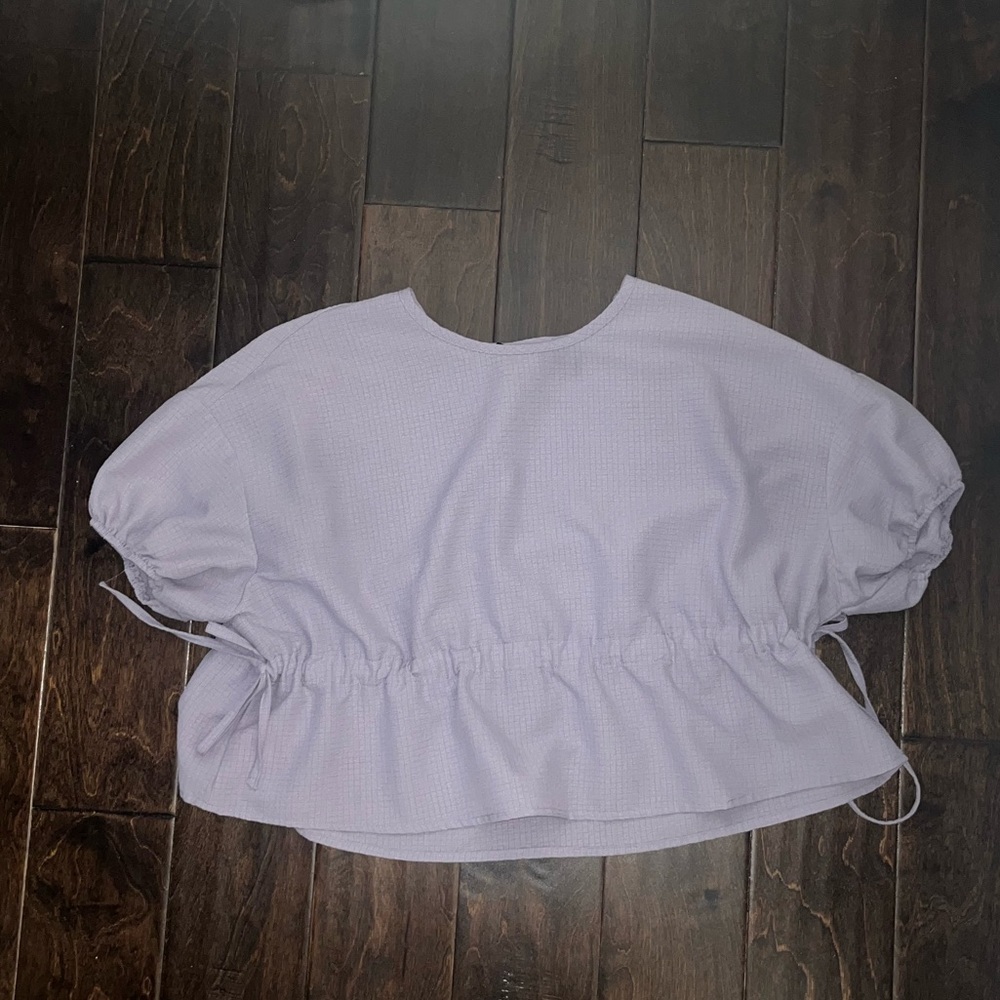 A lavender colored top with drawstrings on the side to adjust tightness of waist
